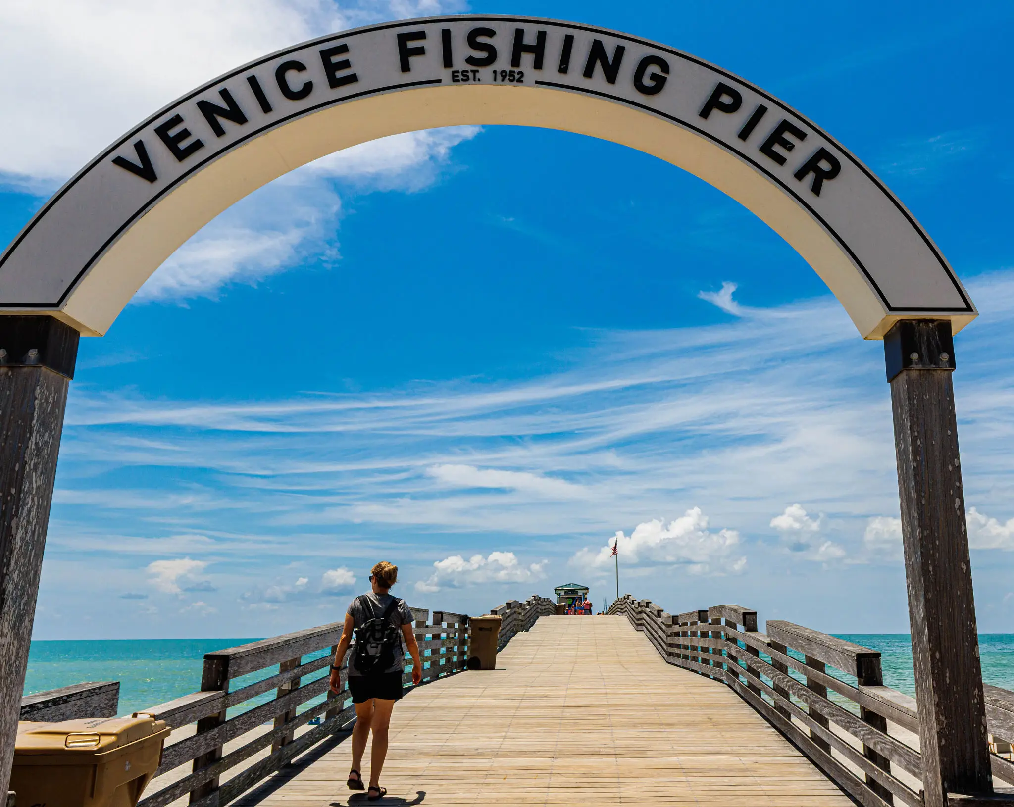 Person walking on Venice Fishing Pier under a blue sky.
