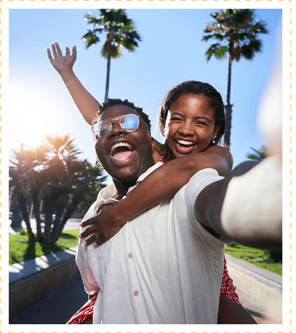Happy couple taking a joyful selfie outdoors on a sunny day.