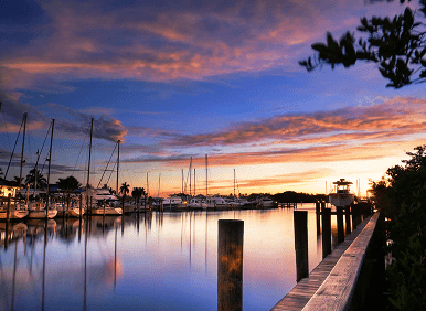 Sunset over a serene marina with sailboats and calm water.