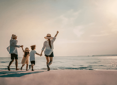 A family joyfully walks hand-in-hand along the beach at sunset.